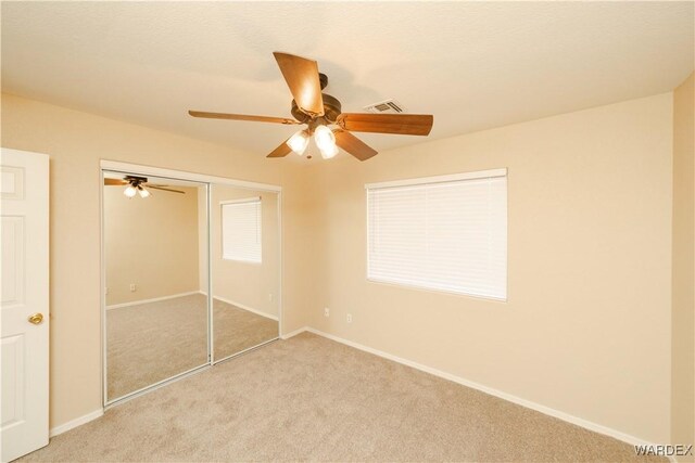 unfurnished bedroom featuring ceiling fan, a closet, baseboards, and light colored carpet