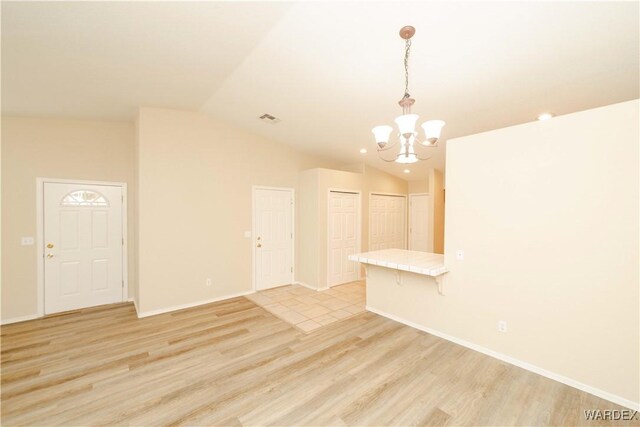 unfurnished room featuring light wood-type flooring, lofted ceiling, a notable chandelier, and baseboards