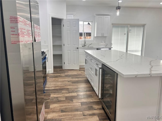 kitchen with light stone counters, beverage cooler, a sink, white cabinetry, and freestanding refrigerator