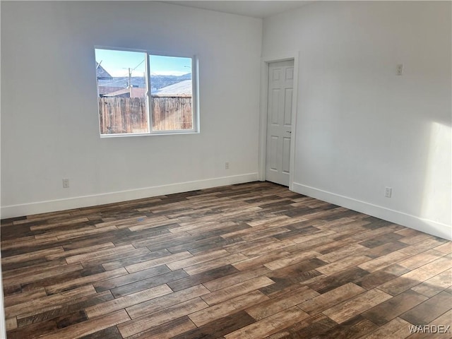 spare room featuring dark wood-style floors and baseboards