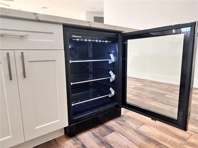 details featuring wine cooler, white cabinets, and wood finished floors