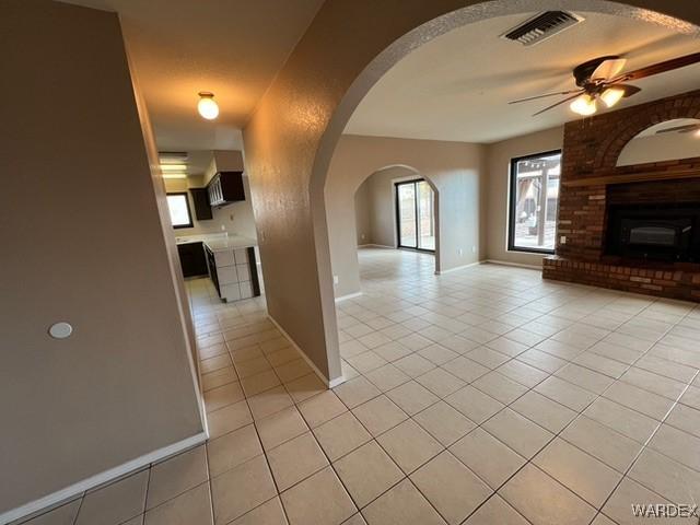 unfurnished living room featuring light tile patterned floors, ceiling fan, visible vents, and arched walkways