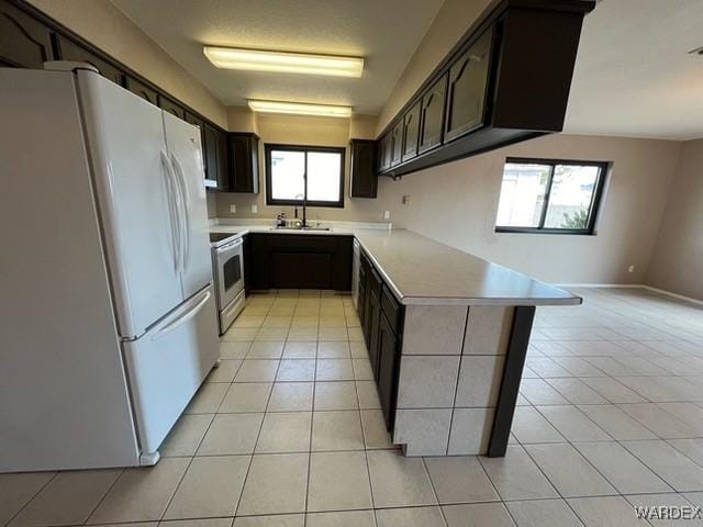 kitchen featuring light tile patterned floors, light countertops, a sink, white appliances, and a peninsula