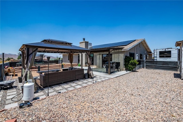 rear view of property featuring solar panels, a patio, an outdoor hangout area, fence, and a gazebo