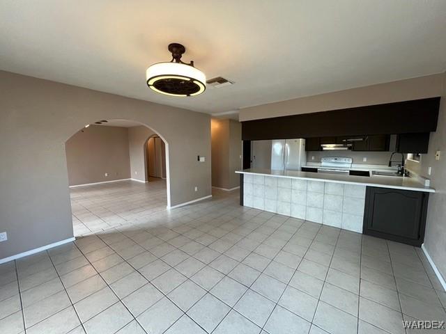 kitchen with range with electric stovetop, light countertops, visible vents, freestanding refrigerator, and a sink