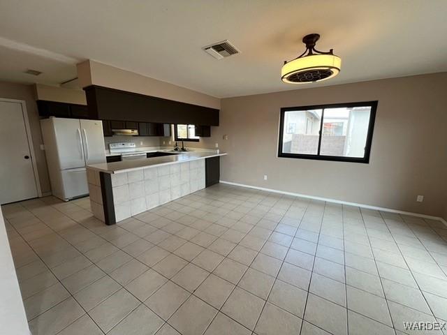 kitchen with white appliances, visible vents, open floor plan, a peninsula, and light countertops