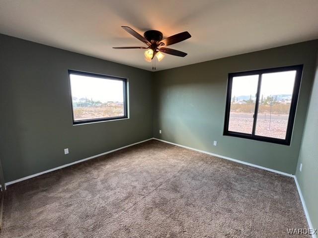 carpeted spare room featuring baseboards, ceiling fan, and a healthy amount of sunlight