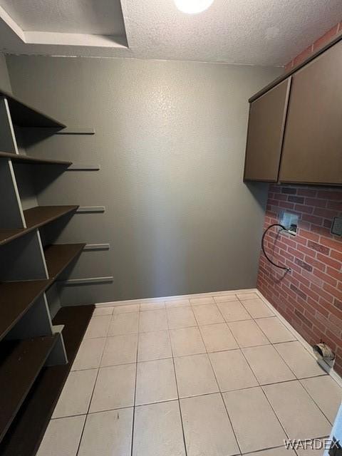 interior space with a textured ceiling, brick wall, and light tile patterned floors