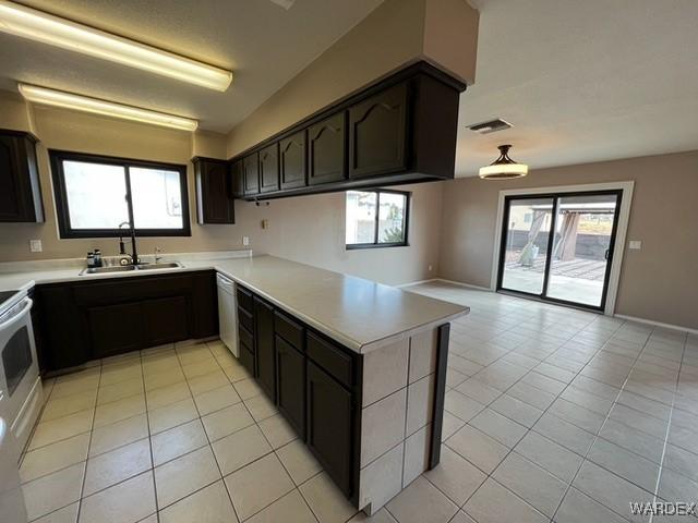 kitchen featuring dark brown cabinetry, visible vents, a peninsula, light countertops, and a sink