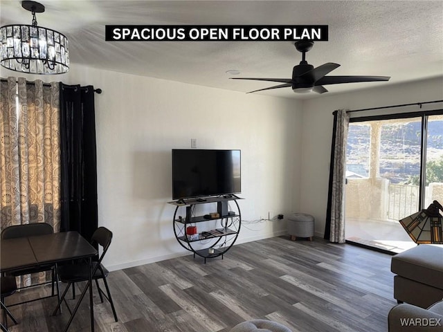 living area with dark wood-style floors, a textured ceiling, ceiling fan with notable chandelier, and baseboards