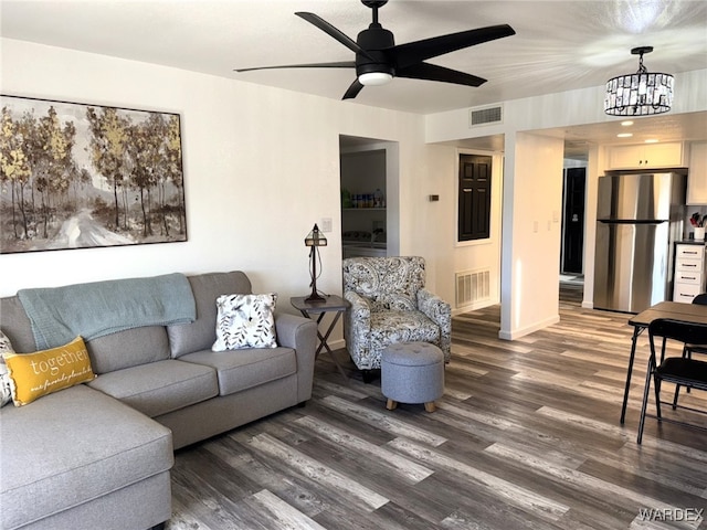 living area featuring dark wood-style floors, ceiling fan with notable chandelier, visible vents, and baseboards