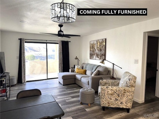 living room with dark wood-type flooring, a textured ceiling, baseboards, and ceiling fan with notable chandelier