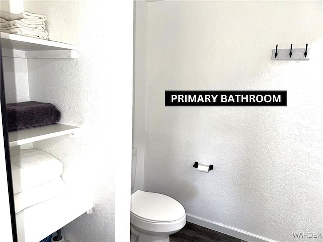 half bath with baseboards, a textured wall, toilet, and wood finished floors