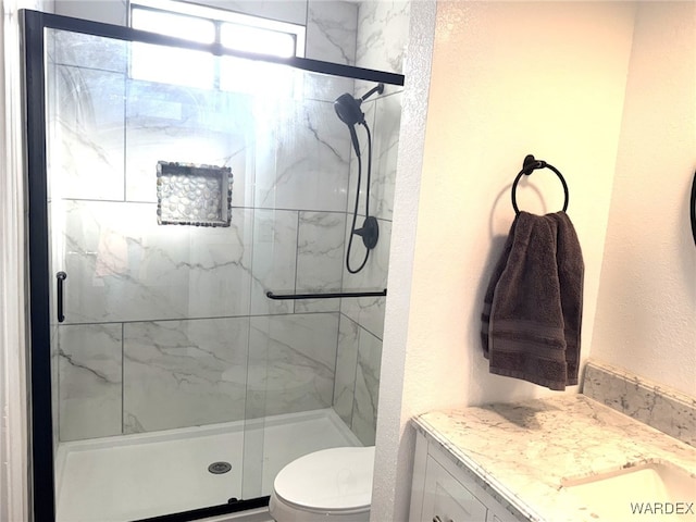 bathroom featuring toilet, a textured wall, vanity, and a marble finish shower