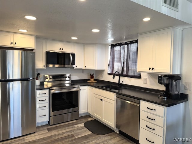 kitchen featuring stainless steel appliances, dark countertops, visible vents, white cabinets, and a sink