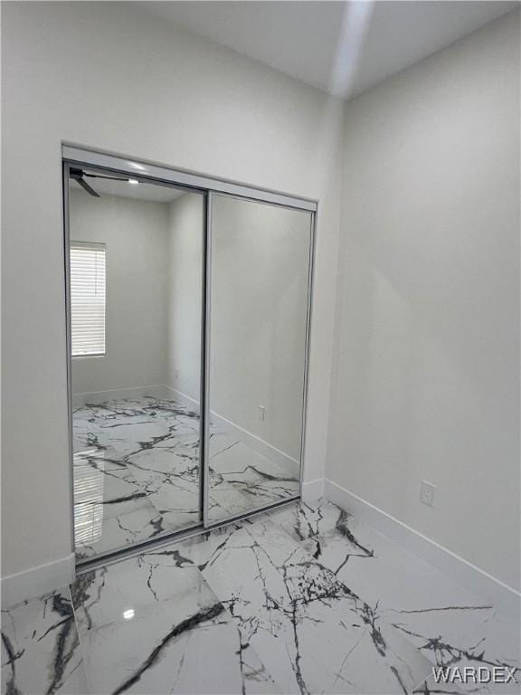 unfurnished bedroom with marble finish floor, a closet, and baseboards