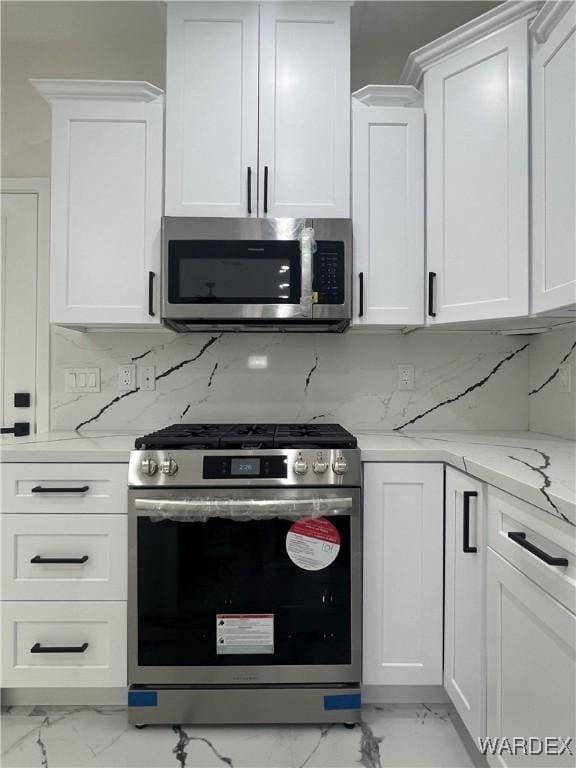 kitchen featuring appliances with stainless steel finishes, marble finish floor, white cabinetry, and light stone counters