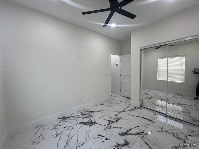 unfurnished bedroom with marble finish floor, ceiling fan, baseboards, and a closet