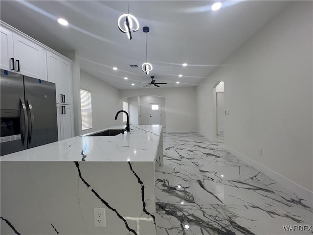 kitchen with arched walkways, white cabinets, light stone counters, pendant lighting, and stainless steel refrigerator with ice dispenser