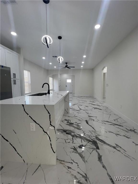 kitchen featuring a kitchen island with sink, a sink, white cabinetry, hanging light fixtures, and light stone countertops