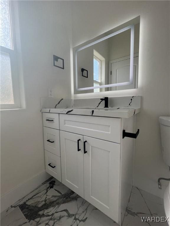 bathroom with toilet, marble finish floor, vanity, and baseboards