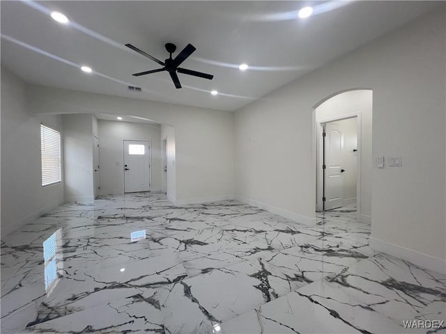 unfurnished living room with arched walkways, marble finish floor, visible vents, ceiling fan, and baseboards