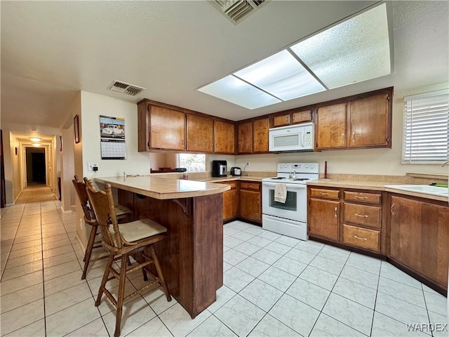 kitchen featuring visible vents, a peninsula, brown cabinetry, white appliances, and a sink