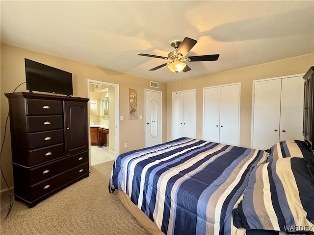 bedroom with visible vents, ensuite bath, ceiling fan, light carpet, and two closets