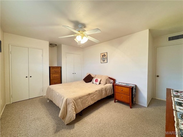 bedroom with visible vents, multiple closets, light colored carpet, and a ceiling fan