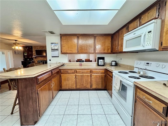 kitchen featuring visible vents, light countertops, a kitchen breakfast bar, a peninsula, and white appliances