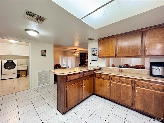 kitchen with washing machine and clothes dryer, visible vents, light countertops, light tile patterned floors, and a peninsula