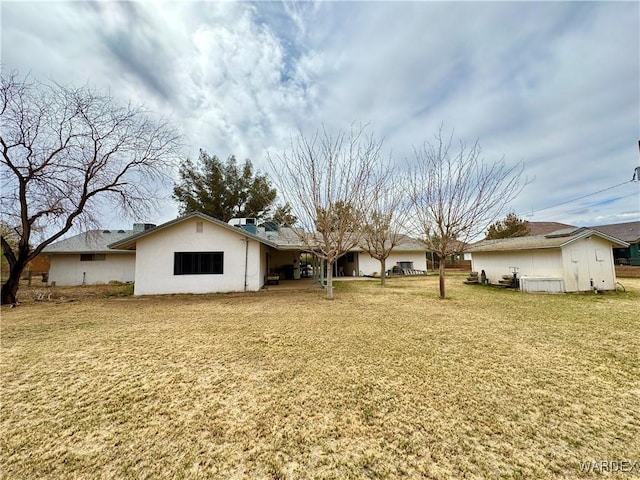 rear view of house with stucco siding and a yard