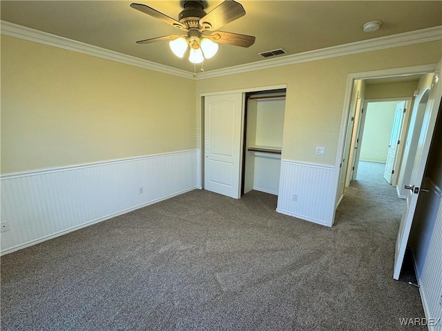 unfurnished bedroom featuring visible vents, ornamental molding, a closet, a wainscoted wall, and carpet