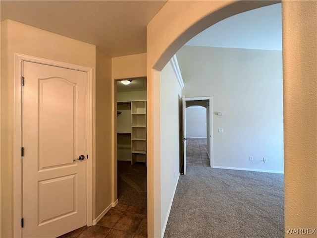 hallway with arched walkways, baseboards, and dark colored carpet