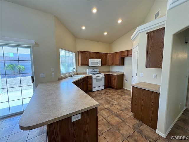 kitchen with visible vents, a peninsula, white appliances, light countertops, and a sink