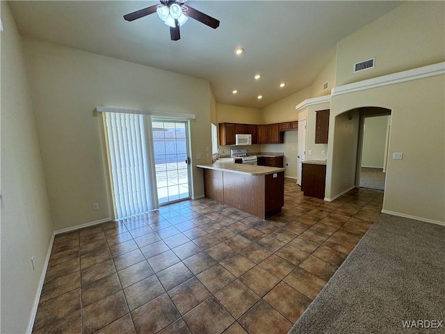 kitchen featuring ceiling fan, arched walkways, stainless steel gas stove, white microwave, and a peninsula