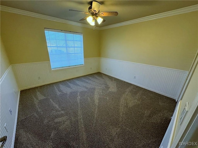 carpeted spare room with crown molding, ceiling fan, and wainscoting