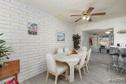 dining area featuring brick wall, wood finished floors, and a ceiling fan