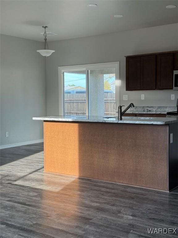 kitchen featuring pendant lighting, dark wood finished floors, a sink, dark brown cabinetry, and baseboards