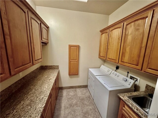 washroom featuring light tile patterned floors, a sink, baseboards, cabinet space, and washer and clothes dryer