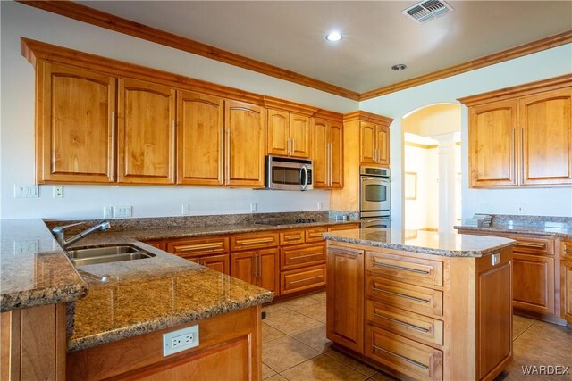 kitchen with visible vents, arched walkways, a kitchen island, stainless steel appliances, and a sink