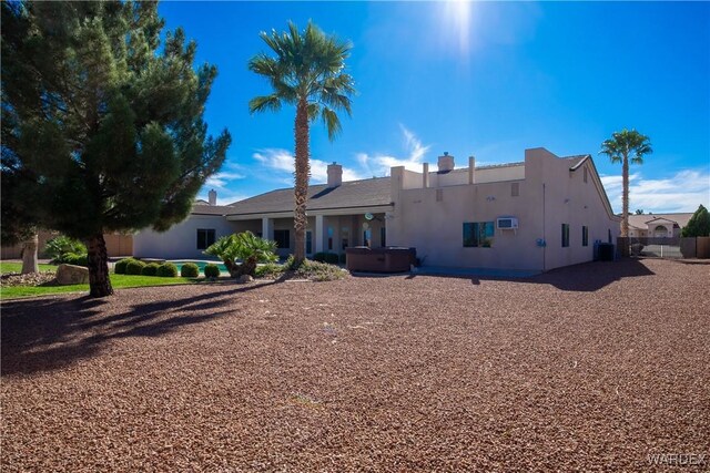 rear view of house featuring stucco siding, fence, and a hot tub