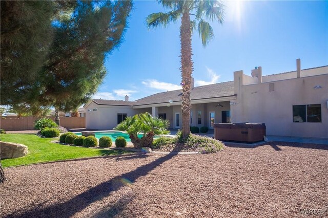 rear view of property featuring a hot tub, a swimming pool, fence, and stucco siding