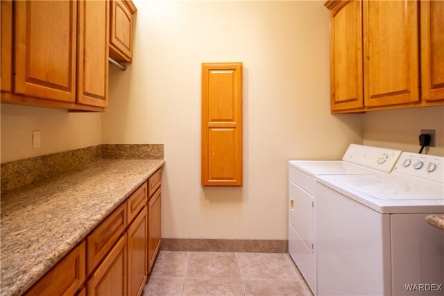 washroom with washing machine and dryer, cabinet space, baseboards, and light tile patterned floors