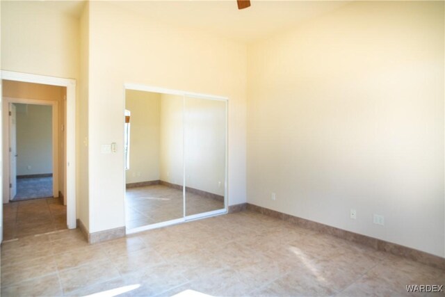 unfurnished bedroom with a high ceiling, baseboards, and a closet