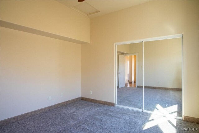 unfurnished bedroom featuring attic access, carpet, a high ceiling, and baseboards