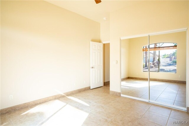 unfurnished bedroom with a high ceiling, baseboards, a closet, and light tile patterned flooring