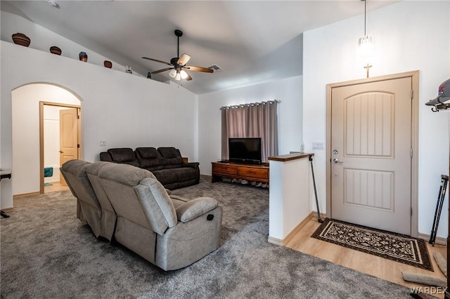 living area featuring a ceiling fan, arched walkways, vaulted ceiling, and carpet