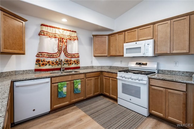 kitchen with light stone countertops, a sink, light wood-style flooring, and white appliances