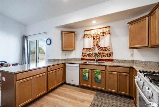 kitchen featuring a sink, light wood-style floors, light stone counters, a peninsula, and white appliances
